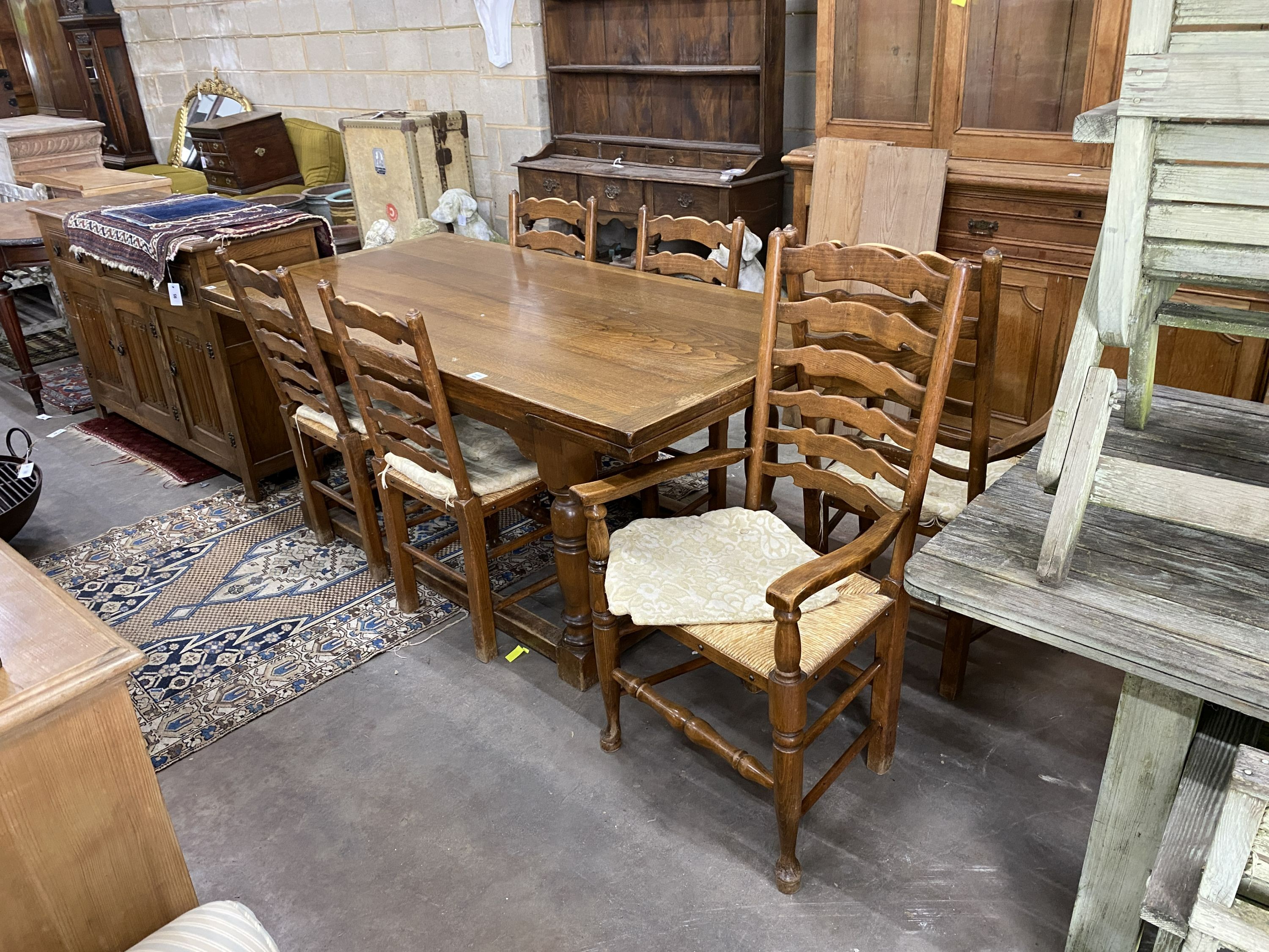 An 18th century style oak dining suite comprising extending draw leaf refectory table, 243cm extended, width 90cm, height 76cm, six rush seat ladder back chairs, two with arms and a linenfold moulded sideboard